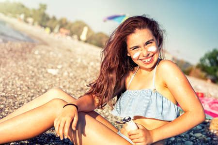 Young teenager girl summer day on the sea beach applying sunblock sunscreen cream