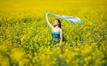 Nice young woman with closed eyes standing in yellow blooming rapeseed field