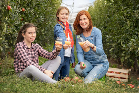 Smiling young family with 100% organic apple juice in apple orchard