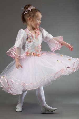 Little girl dancing in studio wearing light chiffon dress, over gray backgroundの写真素材