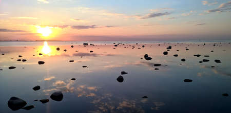 Beautiful sunset over sea with reflection of clouds and rocksの写真素材