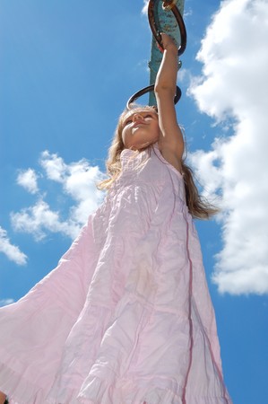  5 year old girl hanging on gymnastic rings moving along the monkey bars against the blus sky