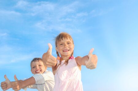 happy 5-6 year old boy and girl with their thumbs up against the blue skyの写真素材