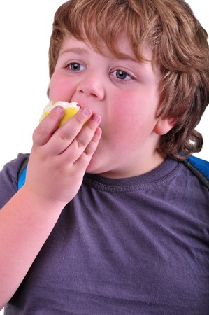 Closeup ortrait of cute schoolboy eating apple. Isolated over white backgroundの写真素材