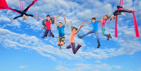 Group happy dancing jumping and aerial silks performing together children in blue sky. の写真素材