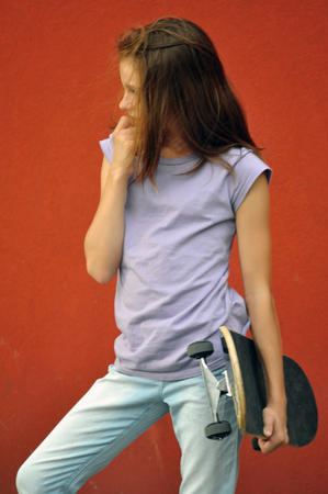 Young teenage girl with skateboard in the street. Red grunge background.の写真素材