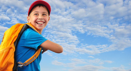 happy smiling choolkid  with backpack against blu cloudy skyの写真素材