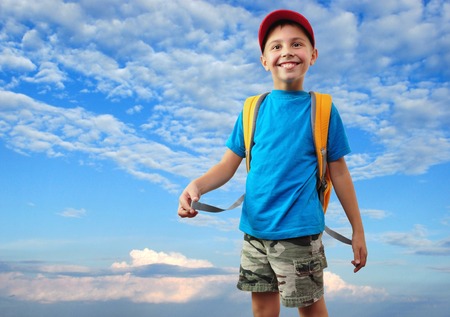 happy smiling schoolkid  with backpack against blue cloudy skyの写真素材