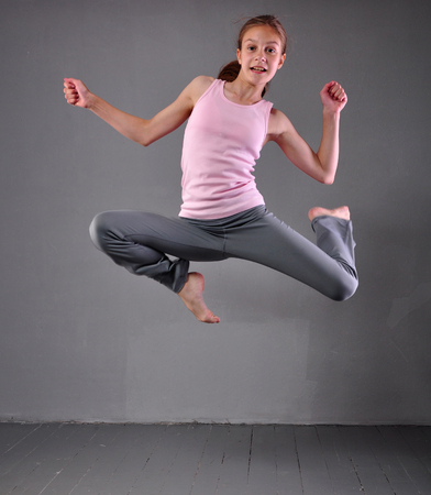 Healthy young muscular teenage girl dancer skipping jumping and dancing in grey studio. Child exercising. Sport healthy lifestyle concept. Sporty childhood.の写真素材