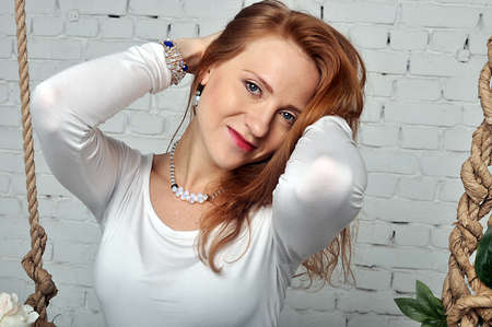 Girl in a white jacket with red hair holding her hands behind her headの写真素材