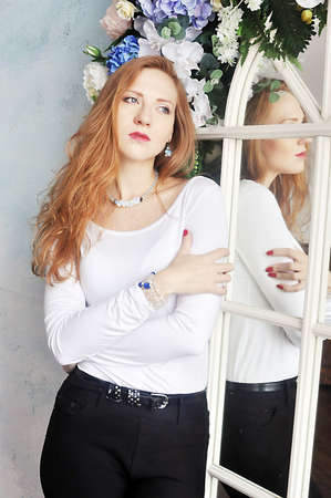 Beautiful fashionable red-haired girl standing near a mirrorの写真素材