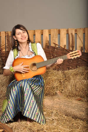 Cheerful young girl playing guitar in the hayloftの写真素材