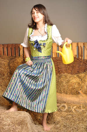 Girl in a dress is smiling holding a watering can in the hayloftの写真素材