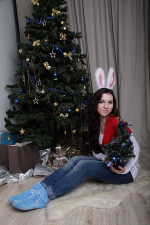 Girl with rabbit ears sitting beside Christmas treeの写真素材