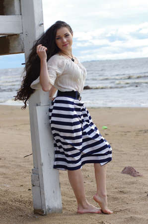 Beautiful young girl with long dark hair standing barefoot on the beachの写真素材