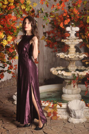 Beautiful girl in a purple dress standing near the fountainの写真素材