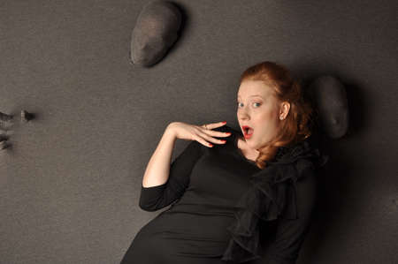 Emotional red-haired girl in a black dress standing near the wallの写真素材