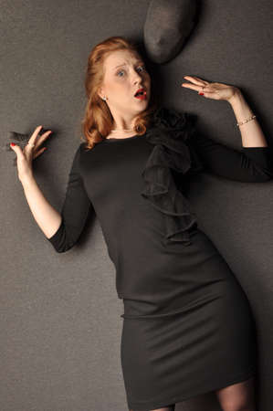Emotional red-haired girl in a black dress standing near the wallの写真素材