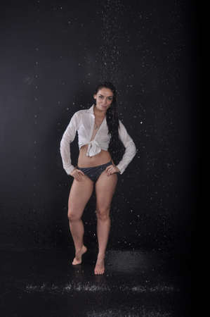A girl in a white shirt dancing barefoot in the rain on a black backgroundの写真素材