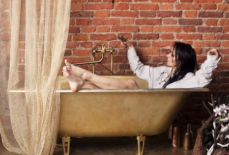 A girl sitting in a gold bath with a shower in hand and barefoot restingの写真素材