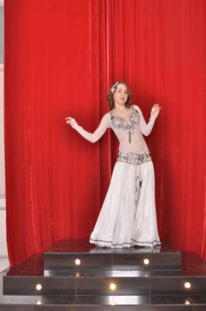 Girl in white oriental costume dancing belly dance on red backgroundの写真素材