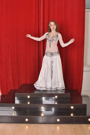 Girl in white oriental costume dancing belly dance on red backgroundの写真素材
