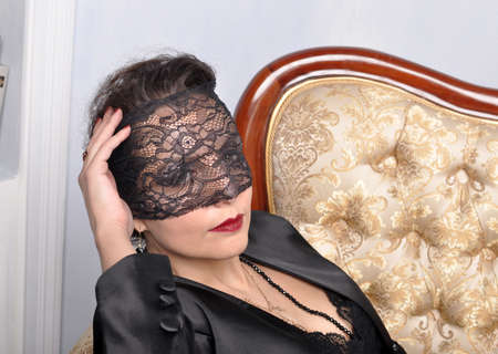 A girl in a black mask resting on a golden sofaの写真素材