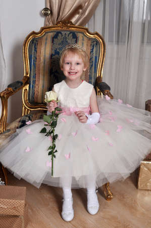 Little girl in a white dress with a rose in her handsの写真素材