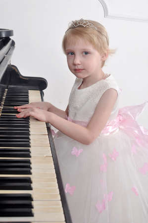 Little girl in white dress playing the pianoの写真素材