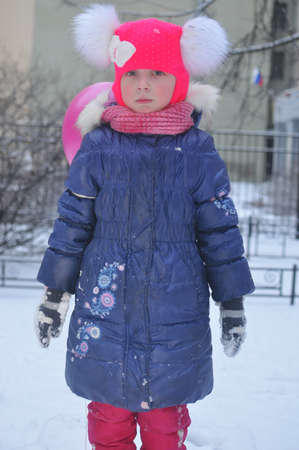 A girl in a pink hat in winter on a walkの写真素材