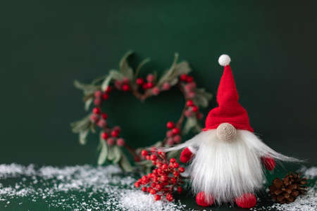 Christmas gnome with winter berry, pine and omela on dark green background. New year greeting card...