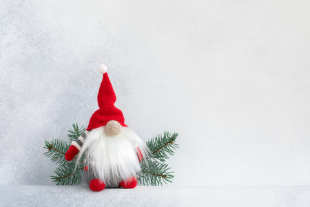 Christmas gnome in red cap with fir branch holiday invitation card on light winter backgroundの写真素材