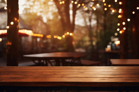 Empty wooden cafe table with a soft focus on the festive blurred lights hanging from the trees. Cozy evening at restaurant conceptの素材