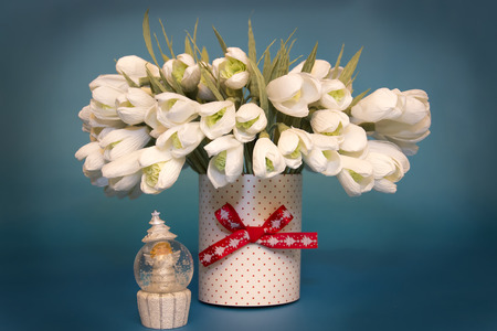 vase with artificial snowdrops isolated on blue with a toy angelの写真素材