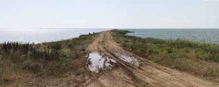 isthmus between the sea with the city on the horizon. dirt road with puddle and mud. on the horizon of the city.の写真素材