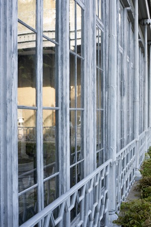 background of large stained glass Windows. frames are white. in the reflection of houses, trees. front Windows, green plants. large Windows of a large house. the frames are peeling paint. the Windows are fenced with a white gridの写真素材