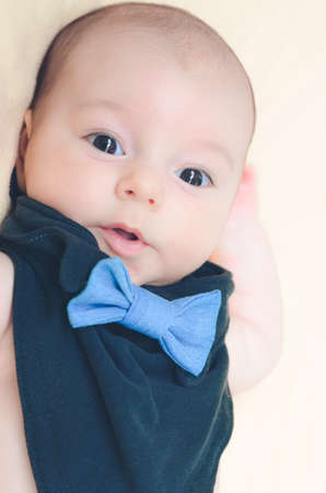 The baby in a black bib with a denim bow tie looks in surprise at the camera lens with his mouth slightly open .the background is blurredの写真素材