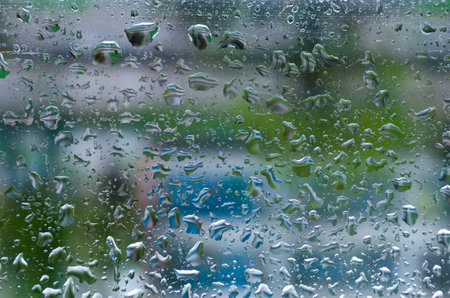 large and small drops of water on the glass of an uneven shape .the background is blurred .there is a green and blue color.の写真素材