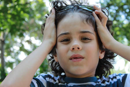 Portrait of a beautiful curly child who holds with both hands on his head