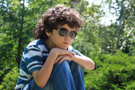 Portrait of a beautiful curly boy sitting with head propped on his kneesの写真素材