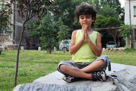 Little curly boy doing yoga in the parkの写真素材