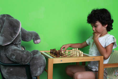 Happy little boy is playing chess with his toy elephant friend at homeの写真素材