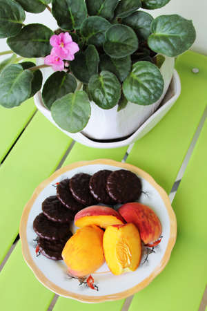 Plate with delicious peach and chocolate cookies on green table with fresh violetsの写真素材