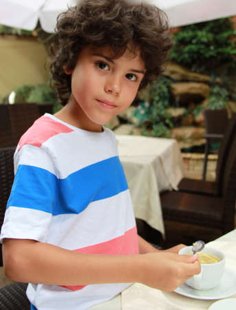 Beautiful boy with curly hair is stirring his teaの写真素材