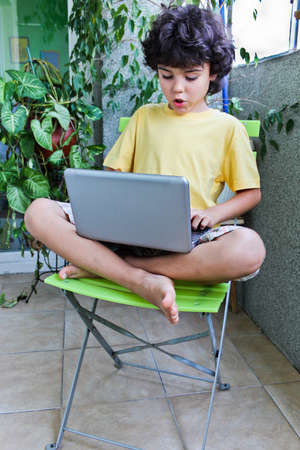 A boy sitting on the green chair and working on  his laptopの写真素材