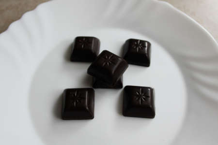 Black chocolate candies in white plate, isolated