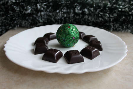 Christmas decoration with dark chocolate and green festive ball in white plateの写真素材