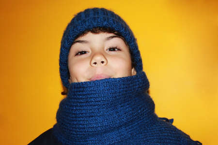 Little boy with knitted hat and scarf on yellow backgroundの写真素材