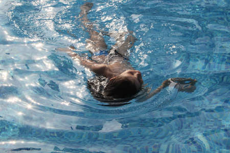Little boy with long hair swims in a blue swimming poolの写真素材