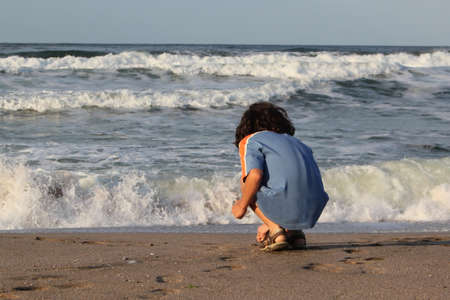 Cute little boy on the beach in front of the sea wavesの写真素材